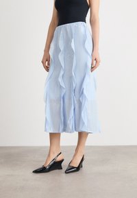 Jupe midi plissée bleu clair avec des couches froncées et un éclat subtil, associée à des talons compensés à brides noires avec des bouts pointus.