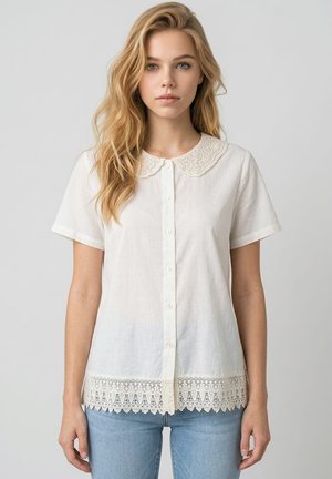 Joven mujer con cabello largo y rubio que lleva una blusa blanca de manga corta con botones, con cuello y dobladillo de encaje, combinada con vaqueros azul claro.