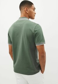 Grøn polo skjorte med korte ærmer, tekstureret stof, kontrasterende stribe detaljer på kraven og ærmerne, samt en afslappet pasform.