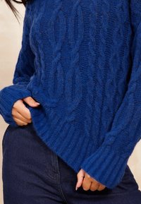 Modra pletena športna majica z rebrastim robom in manšetami, izdelana iz mehkega, teksturiranega materiala, z večjim krojem in vidnimi šivi.