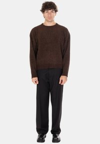 Maglione marrone a maglia con collo rotondo e orlo a coste, abbinato a pantaloni neri e scarpe nere. La texture sembra morbida e informale.