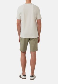 Korte mouwen, lichtbeige gestructureerd t-shirt gecombineerd met olijfgroene shorts. Dragen met casual zwarte en witte sneakers.