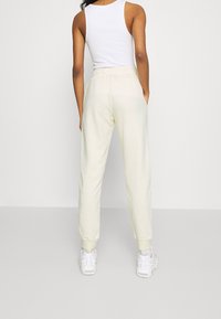 Cream-colored sweatpants with a tapered fit, elastic waistband, and cuffed ankles. Paired with white sneakers and a fitted white tank top.