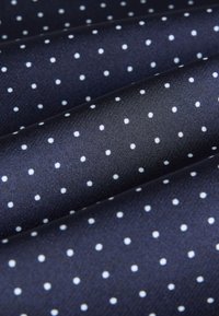 Granatowa tkanina w białe kropki, gładka tekstura i diagonalne fałdy. Każda kropka jest równomiernie rozmieszczona na materiale.