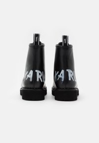 Botas de cuero negras hasta el tobillo con suela gruesa, presentando letras blancas en negrita "KARL" en los lados y tiradores para facilitar el uso.