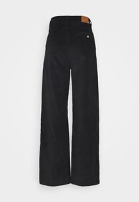 Zwarte corduroy wijde broek met een gestructureerde afwerking, voorzien van een bruine leren patch aan de achterkant van de taille en een enkele achterzak.