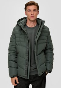 Donkergroene pufferjack met een capuchon, voorzien van horizontale gestikte panelen, een rits aan de voorkant en een drukknoopsluiting. Textuurstof met een matte afwerking.