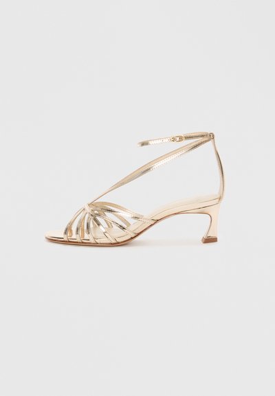 Gold transparent heeled sandal with a strappy design, open-toe, and a slender mid-heel. Features a buckled ankle strap.