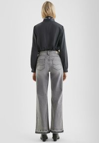Schwarze Button-up-Bluse mit einem gemusterten Kragen, kombiniert mit hoch taillierten grauen Schlagjeans, die einen ausgefransten Saum und zwei Gesäßtaschen haben.