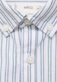 Cămașă albă, cu dungi verticale albastre deschise, având un guler clasic și nasturi din plastic. Țesătura pare texturată și țesută.