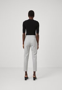 Črn oprijet zgornji del s kratkimi rokavi v kombinaciji z svetlo sivimi krojenimi hlačami. Hlače imajo subtilen vzorec in zožen kroj. Črne salonarje.