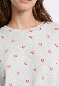 Camisa corta de manga corta en gris claro con escote redondo, que presenta pequeños patrones de corazones rosas en toda la tela. Textura suave y diseño informal.