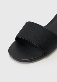 Svart slide-sandal med ett brett, strukturerat rem och en slät sula. Designen är minimalistisk med en platt sula.