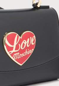Black leather bag with gold-trimmed red heart emblem featuring white script text "Love Moschino" on the front flap.