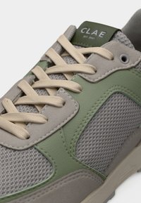 Μπεζ και πράσινο αθλητικό παπούτσι με πάνελ από δίχτυ και σουέτ, μπεζ κορδόνια και το λογότυπο "CLAE" στη γλώσσα.