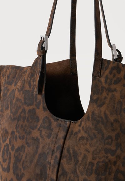 Sac fourre-tout en daim marron avec motif léopard foncé et deux fines bretelles d'épaule fixées par des boucles rectangulaires argentées.