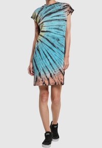 Sukienka tie-dye o spiralnym wzorze w kolorach niebieskim, różowym i czarnym. Krótkie rękawy, luźny krój, wykonana z miękkiego materiału. W zestawie z czarnymi trampkami za kostkę.