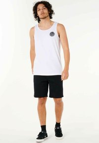 Weißes ärmelloses Tanktop mit einem runden schwarzen Grafikdesign, kombiniert mit schwarzen Shorts und schwarzen Sneakers. Glatter Stoff, lässige Passform.