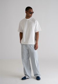White cotton t-shirt with a loose fit, paired with light blue and white striped wide-leg pants, completed with navy-blue shoes.