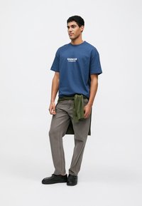 Blue cotton t-shirt with "BARBOUR INTERNATIONAL" text, paired with olive green pants and black shoes. Simple design, relaxed fit.