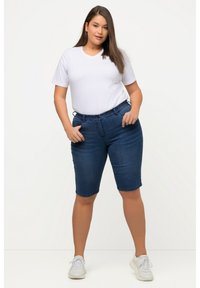 Bermuda en denim bleu foncé avec une taille élastique, des poches latérales et une coupe ajustée. Associé à un t-shirt blanc à col en V.