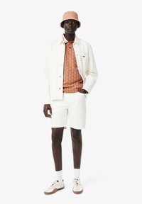 Chaqueta de denim blanca, camisa con estampado terracota, pantalones cortos blancos, zapatillas crema con detalles marrones y un sombrero tipo bucket rosa claro.