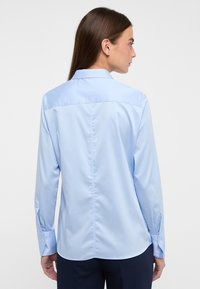 Camicia a maniche lunghe azzurro chiaro con colletto classico, polsini abbottonati e una texture liscia. Presenta un dettagliato cucitura centrale dritta sul retro.