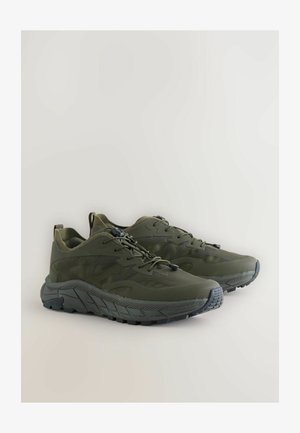 Zöld sportcipők, texturált hálós felsőrésszel, gumitalppal és párnázott nyakkal. Szabályozható illeszkedést biztosító biztosított fűzőrendszerrel rendelkezik.