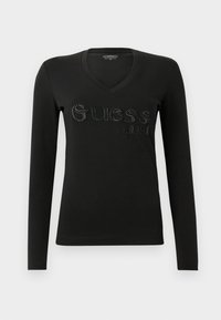 Juodas ilgomis rankovėmis V formos iškirptės marškinėliai su iškilniu "Guess" logotipu ir įsteigimo metų 1981, pasižymintys gležna tekstūra ir prigludusia išvaizda.