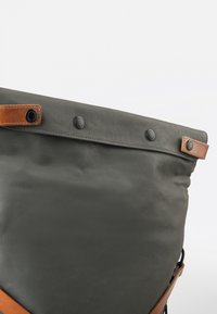 Dunkelgraue Canvas-Tasche mit einem akzentuierten, hellbraunen Lederdetail. Verfügt über schwarze Druckknopfverschlüsse und eine strukturierte Form. Glatte Textur mit minimalistischen Design.