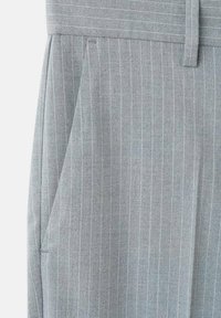 Pantalones grises a rayas con una textura suave, presentan una cinturilla ancha y bolsillos laterales. Las rayas son de un gris claro sobre una base más oscura.