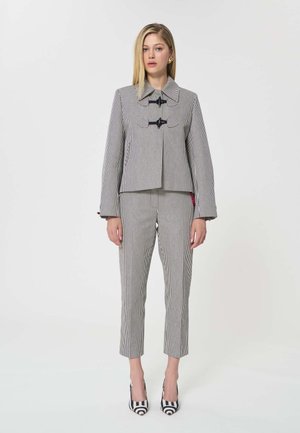 Femme portant un costume à fines rayures verticales noires et blanches avec des fermetures à bascule sur la veste et des escarpins assortis à motif.