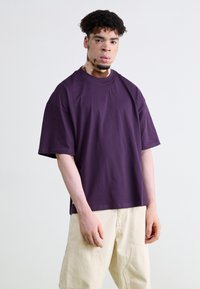Overdimensioneret lilla bomulds t-shirt med rund hals og korte ærmer, båret sammen med beige cargo-shorts, der har en glat tekstur og afslappet pasform.