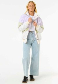 Giacca leggera in blocchi di colore lavanda, bianca e verde, con zip frontale e polsini a coste, abbinata a jeans azzurri a vita alta.