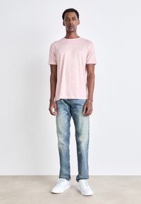 Ljusrosa t-shirt med kort ärm, avslappnad passform, tillsammans med bleka blå jeans och vita sneakers. Slät textur med enkel design.