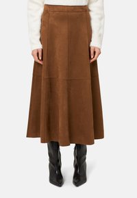 Barna, velúr A-vonalú szoknya, szűk�ített derékkal, varrási részletekkel és hosszú, légies sziluettel, térdig érő fekete csizmával párosítva.