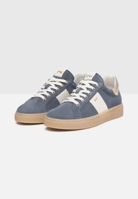 Baskets en daim bleu avec des accents latéraux blancs, des lacets crème et une semelle en caoutchouc beige. Présentent un logo doré sur la languette et un talon doux.