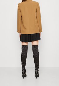 Béžové sako s nařezaným límcem a detailem zadního švu. Kombinováno s černou minisukní a černými kozačkami ke kolenům s nařasením.
