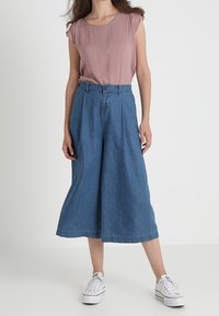 Top a maniche corte con motivo rosso e maniche risvoltate, abbinato a culotte di jeans a gamba larga. L'outfit è completato da sneakers bianche.