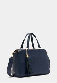 Borsa a mano in pelle blu navy con superficie texturizzata, con dettagli in oro e un pompon staccabile. Presenta due manici e una tracolla.