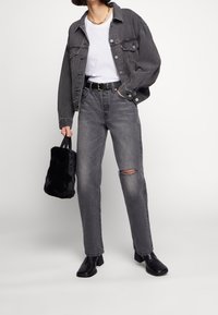 Grå denimjacka och jeans, vit t-shirt, svart bälte och svarta klackstövlar. Inkluderar en liten svart fuskpälsväska. Texturerad tyg, avslappnad passform.