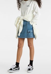 Denimhame, jossa on taskut, vaaleansininen väri, keskipitkä pituus, yhdistetty valkoisen pitkähihaisen paidan ja mustien tennareiden kanssa, valkoinen kerros solmittuna vyötärölle.