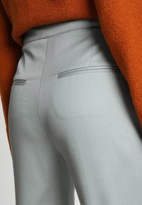 Šedé kalhoty s rovnými nohavicemi mají hladkou texturu, ploché přední kapsy a jemný proužkovaný vzor. Pas je zúžený s úhledným zakončením.