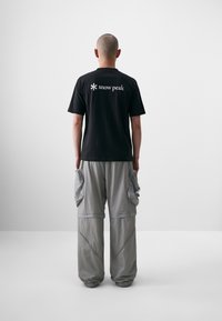 Black cotton t-shirt with "snow peak" logo on the back, paired with light gray cargo pants featuring multiple pockets and a loose fit.