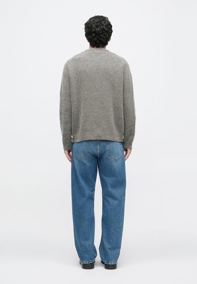 Γκρι πλεκτό ζακέτα με υφή, στρογγυλή λαιμόκοψη και ελαφρώς φουσκωμένα μανίκια, συνδυασμένη με ανοιχτό μπλε φ αρδιά τζιν παντελόνια.