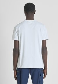 Witte t-shirt met korte mouwen en ronde hals, gladde textuur en rechte achterzoom, gedragen met blauwe cargobroek met zijzakken.