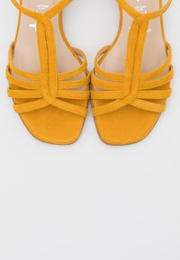 Sandali di suede giallo con un design a strappo, punta aperta e suola piatta, dettagli in cucitura e una fodera interna liscia.