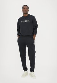 Sort sweatshirt og matchende sweatpants med "Armani Exchange" logo. Materialet ser glat ud og har ribkant ved håndleddene og livet. Hvide sneakers.