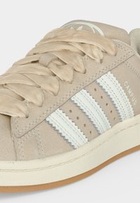 Μπεζ σουέντ αθλητικό παπούτσι με φαρδιές κρεμ κορδονιές, λευκές οδοντωτές ρίγες στο πλάι και το κείμενο «CAMPUS» πάνω από την σόλα.