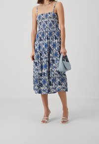 Modrá a bílá květinová midi šaty se smockovaným živůtkem, tenkými ramínky a nařaseným pasem. Doplněné světle modrou kabelkou a bílými lodičkami.